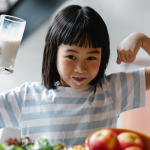 prevenire il rachitismo infantile - bambina orientale con braccia alzate e bicchiere in mano