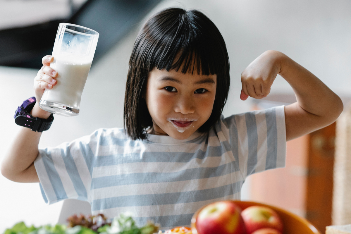 prevenire il rachitismo infantile - bambina orientale con braccia alzate e bicchiere in mano