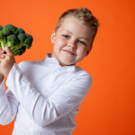 far mangiare frutta e verdura ai bambini - bambino di circa 5 anni sorridente con in mano un broccolo