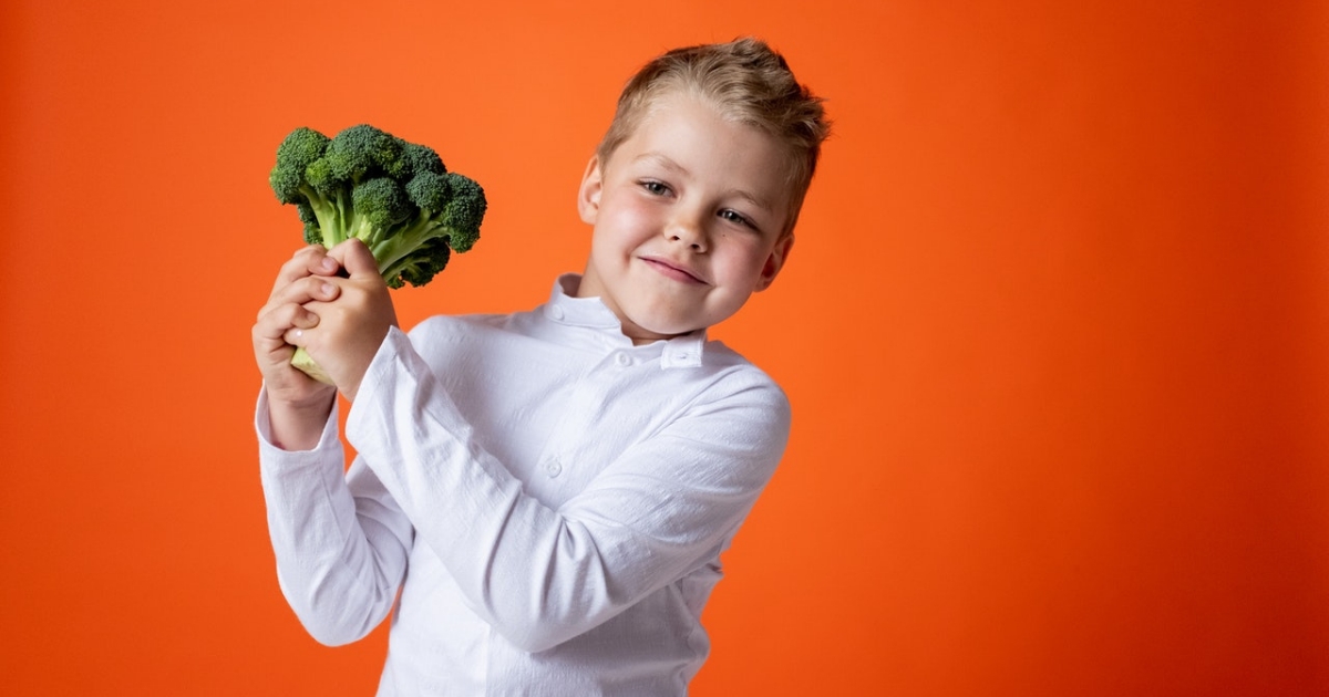 far mangiare frutta e verdura ai bambini - bambino di circa 5 anni sorridente con in mano un broccolo