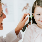 breve guida per pulire le orecchie dei bambini - dottoressa controlla l'orecchio di una bambina sorridente